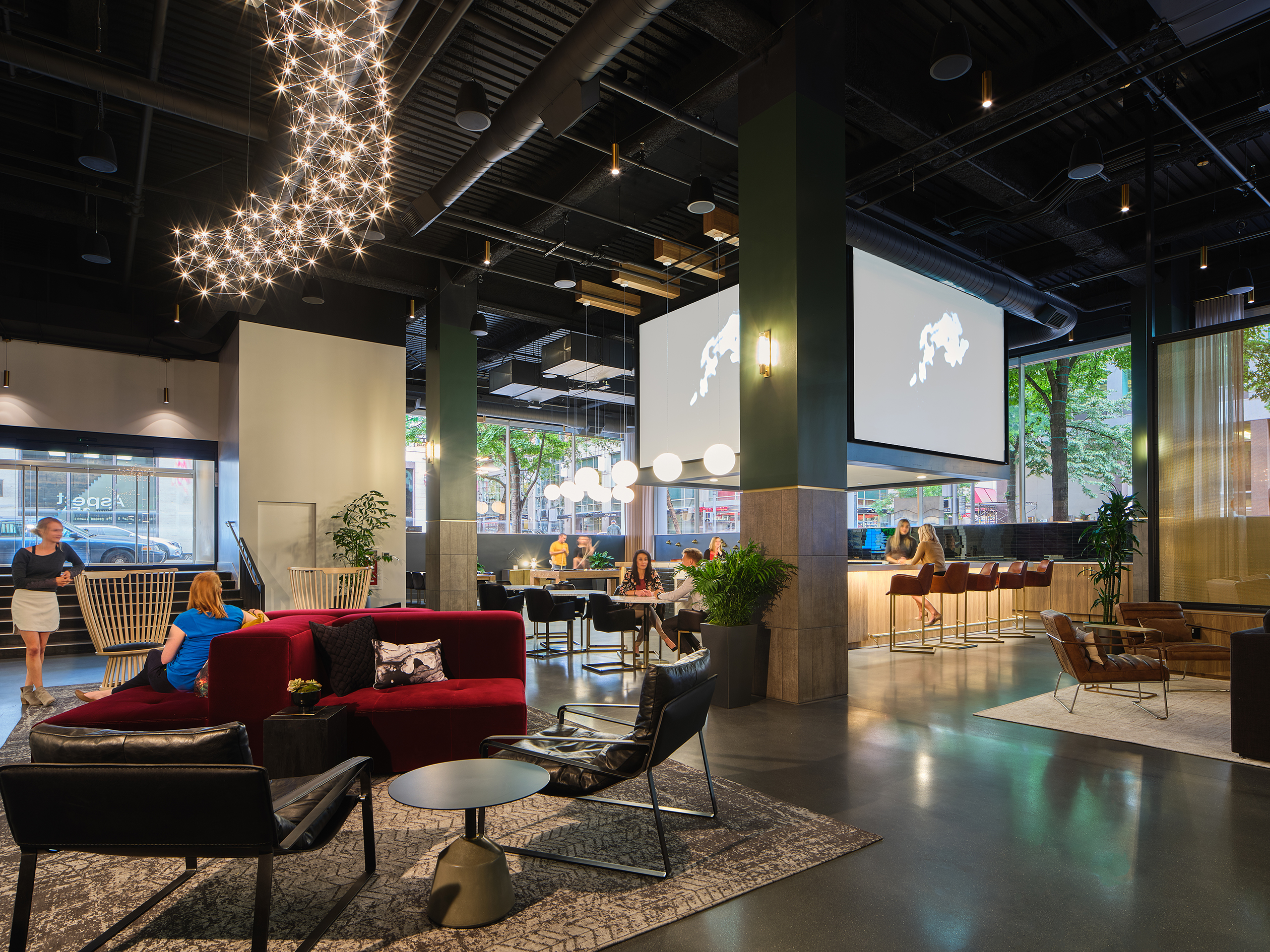 overall lobby view with employees lounging, dual display screens above bar, sofas, light installations and modern seating