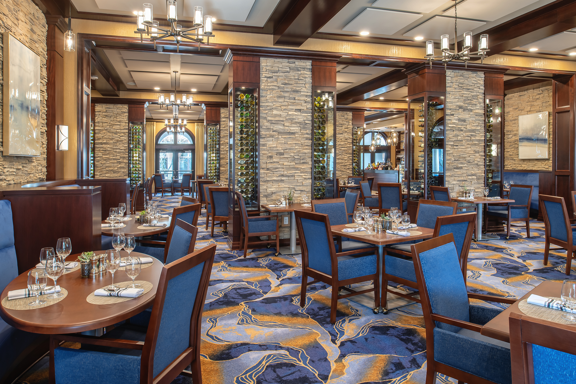seating area of restaurant with colorful accents on chairs, stone, carpeting and wine bottle art decorations
