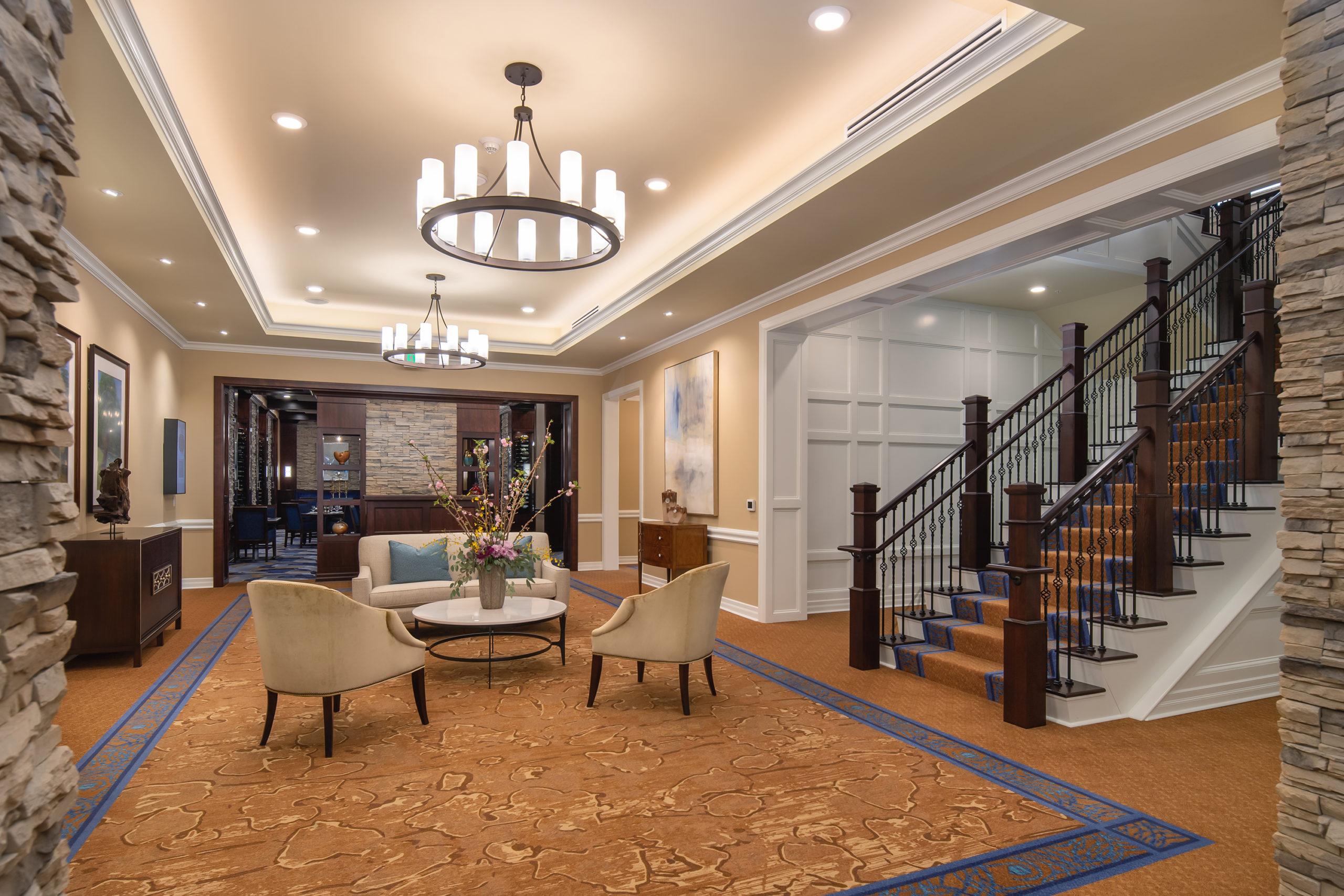 interior waiting area for residents at bottom of staircase, featuring chendeliers, and entrance to restaurant